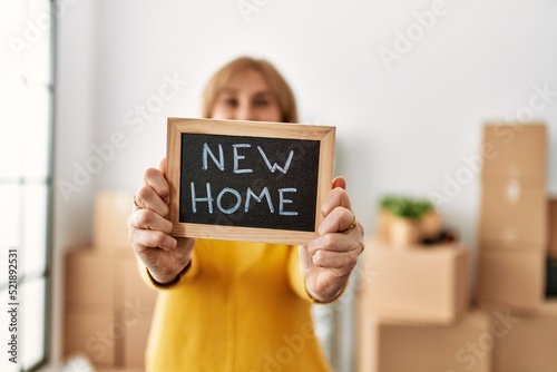 Middle age blonde woman smiling happy holding blackboard with new home message.