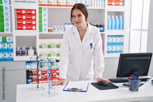 Young woman pharmacist smiling confident standing at pharmacy