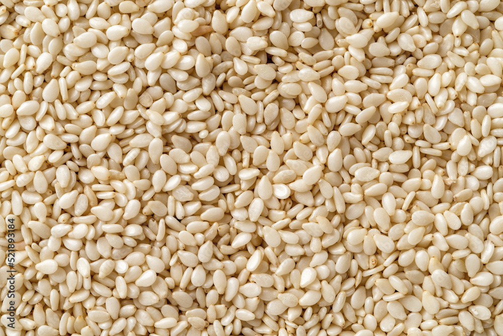 Raw sesame seeds macro background. Texture of organic benne grains closeup. White til for healthy food, strengthening immunity diet and calcium source. Sesamum indicum for oil production. Raw sesame seeds macro background. Texture of organic benne grains closeup. White til for healthy food, strengthening immunity diet and calcium source. Sesamum indicum for oil production.