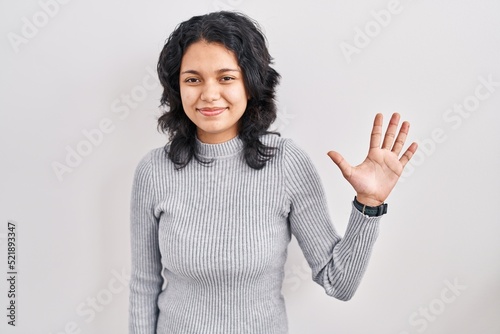 Hispanic woman with dark hair standing over isolated background showing and pointing up with fingers number five while smiling confident and happy.