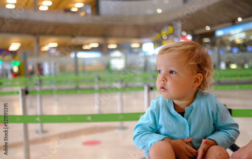 baby at the airport departures terminal patiently sits in the luggage cart.