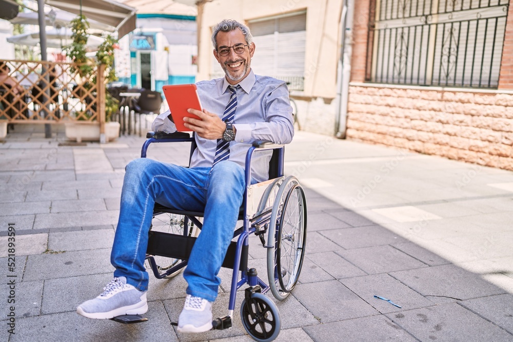 Middle age hispanic man sitting on wheelchair using touchpad at street