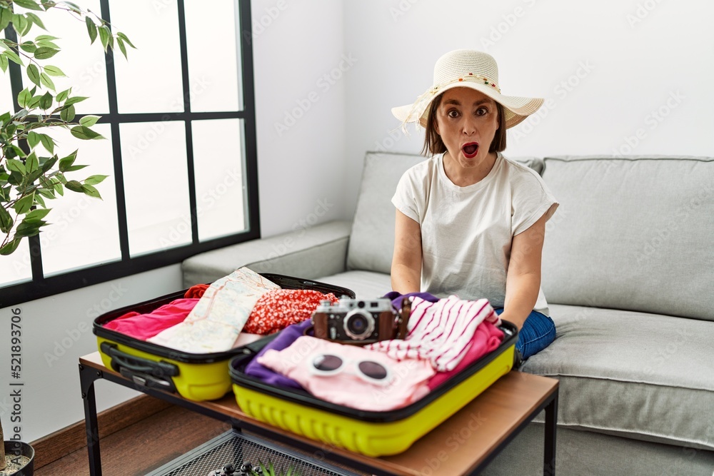 Beautiful middle age hispanic woman packing summer clothes in suitcase