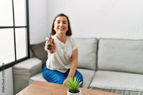 Middle age hispanic woman sitting on the sofa holding new home keys at home