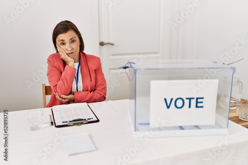 Beautiful middle age hispanic woman at political election sitting by ballot thinking looking tired and bored with depression problems with crossed arms.
