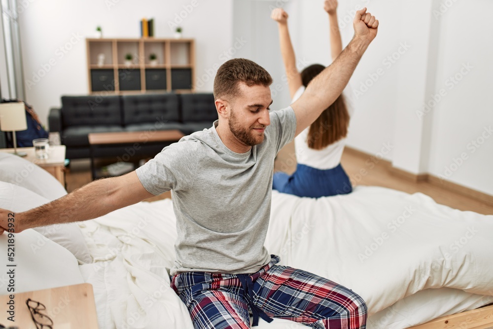Fototapeta premium Young caucasian couple yawning and stretching arms sitting on the bed.