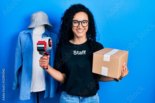 Young hispanic woman with curly hair wearing staff t shirt holding cardboard box smiling with a happy and cool smile on face. showing teeth. photo