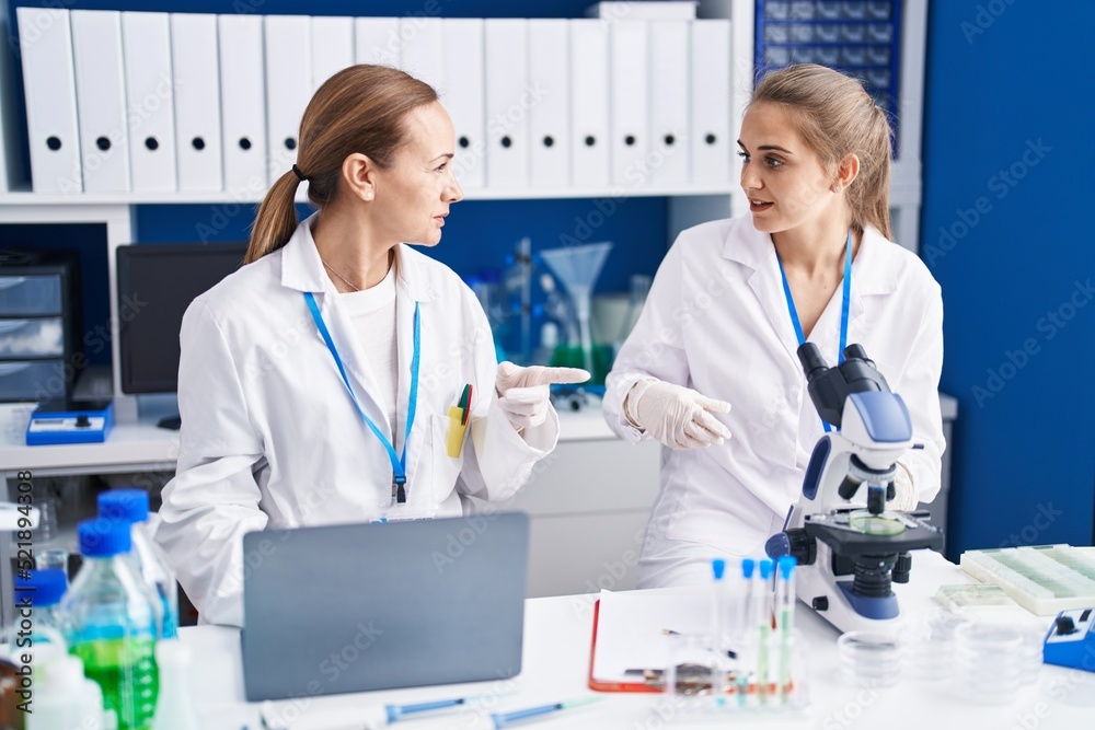 Two women scientists using microscope and laptop at laboratory Two women scientists using microscope and laptop at laboratory