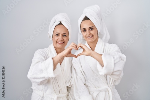 Middle age woman and daughter wearing white bathrobe and towel smiling in love doing heart symbol shape with hands. romantic concept.