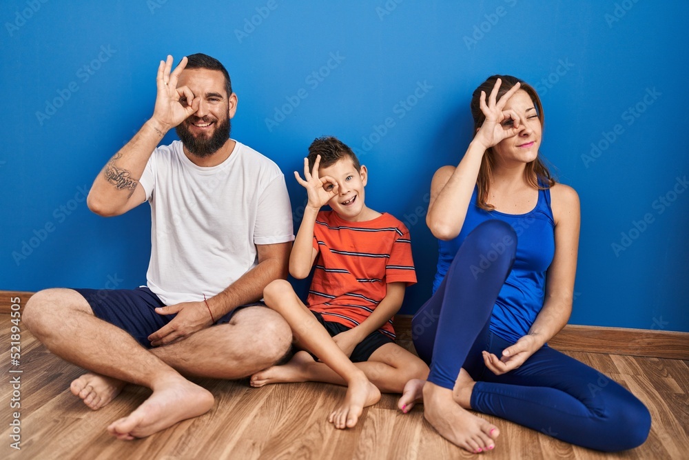 Family of three sitting on the floor at home doing ok gesture with hand smiling, eye looking through fingers with happy face. Family of three sitting on the floor at home doing ok gesture with hand smiling, eye looking through fingers with happy face.