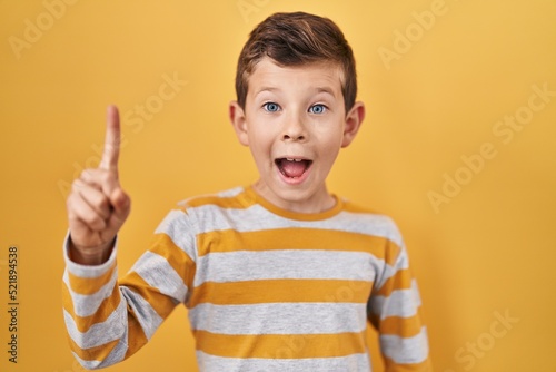 Young caucasian kid standing over yellow background pointing finger up with successful idea. exited and happy. number one.