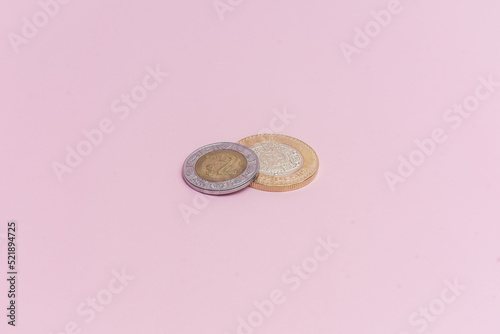 Moneda de 10 pesos mexicanos y moneda de 2 pesos mexicanos sobre fondo rosa.