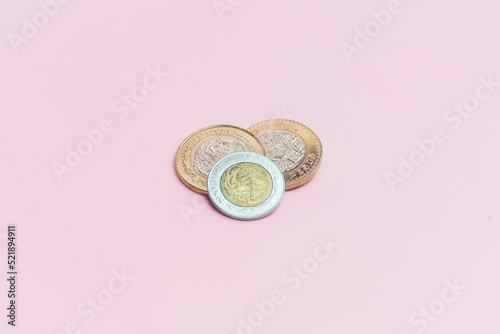 Dos monedas de 10 pesos mexicanos y moneda de 2 pesos mexicanos sobre fondo rosa.