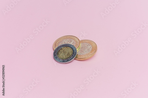 Dos monedas de 10 pesos mexicanos y moneda de 2 pesos mexicanos sobre fondo rosa.