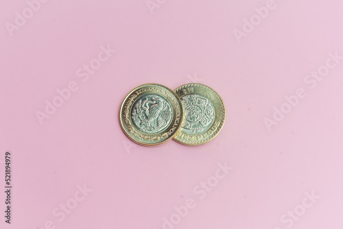 Dos monedas de 10 pesos mexicanos sobre fondo rosa.