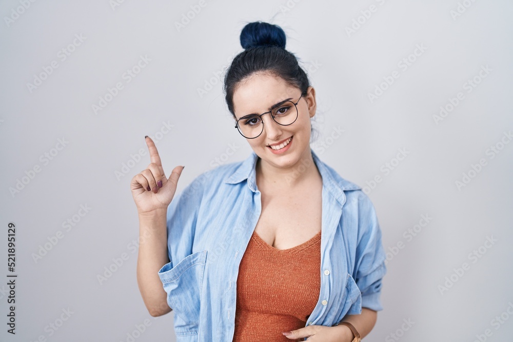 Young modern girl with blue hair standing over white background with a big smile on face, pointing with hand finger to the side looking at the camera. Young modern girl with blue hair standing over white background with a big smile on face, pointing with hand finger to the side looking at the camera.