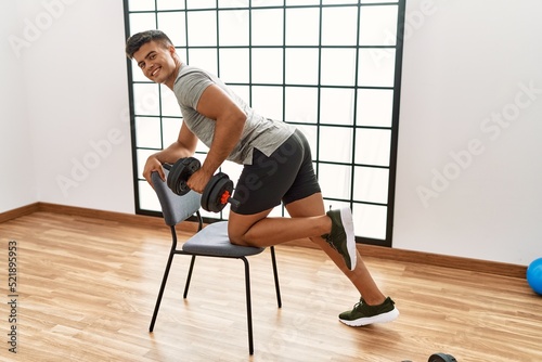 Young hispanic man smiling confident training using dumbbells at sport center