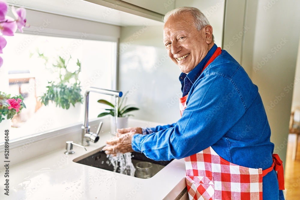 Senior man smiling confident washing hands at kitchen