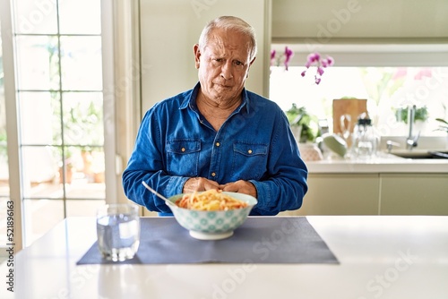 Senior man with grey hair eating pasta spaghetti at home depressed and worry for distress, crying angry and afraid. sad expression.