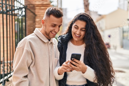 Man and woman couple using smartphone standing together at street