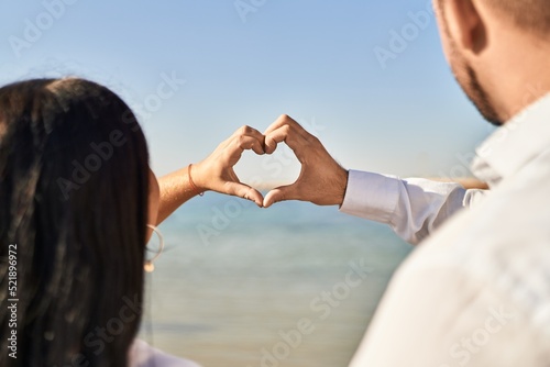 Man and woman couple on back view doing heart symbol with hands at seaside
