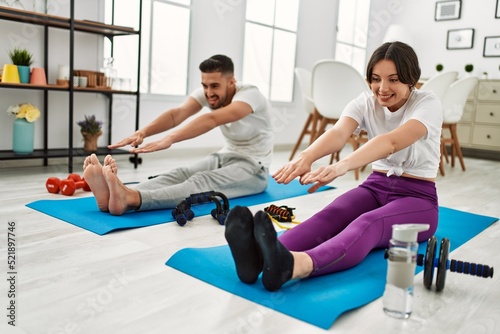 Young hispanic couple doing sport stretching on the mat at home
