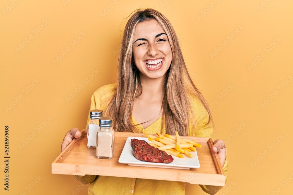 Beautiful hispanic woman holding tray with lunch winking looking at the camera with sexy expression, cheerful and happy face. Beautiful hispanic woman holding tray with lunch winking looking at the camera with sexy expression, cheerful and happy face.