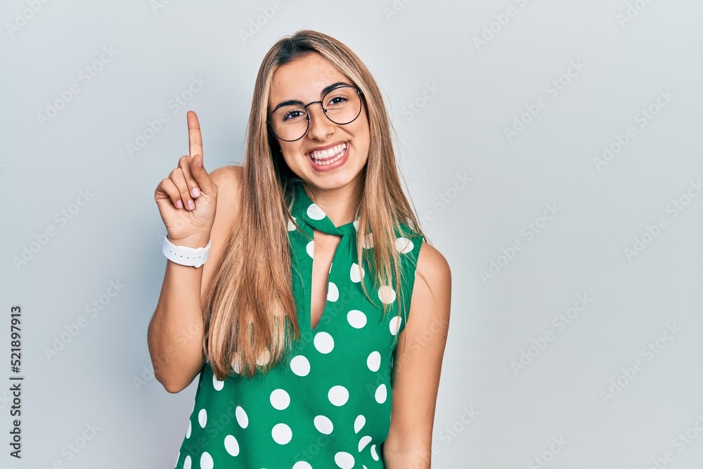 Beautiful hispanic woman wearing elegant shirt and glasses showing and pointing up with finger number one while smiling confident and happy. Beautiful hispanic woman wearing elegant shirt and glasses showing and pointing up with finger number one while smiling confident and happy.