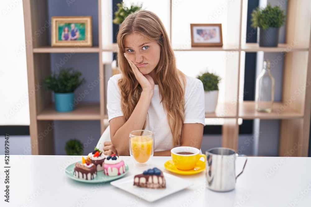 Young caucasian woman eating pastries t for breakfast thinking looking tired and bored with depression problems with crossed arms.