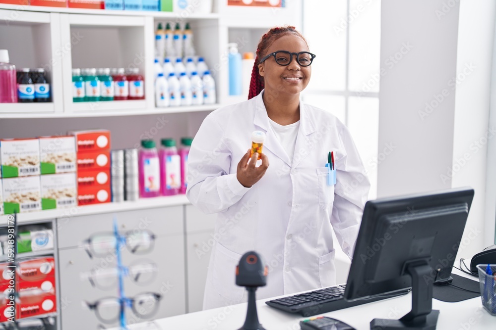 African american woman pharmacist holding pills bottle using computer at pharmacy