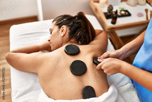 Two women therapist and patient having back massage session using black stones at beauty center