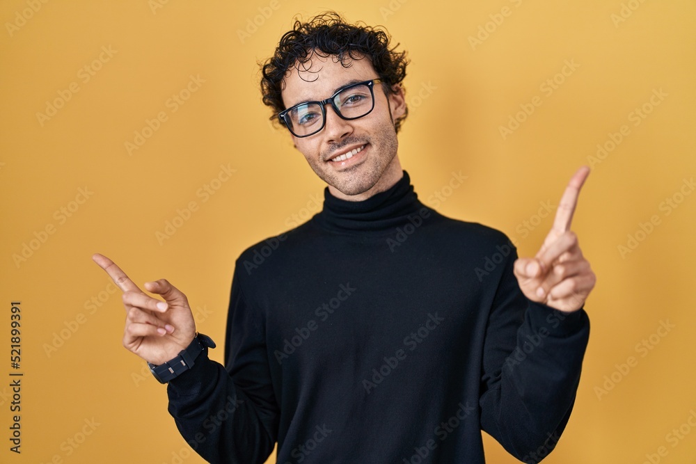Hispanic man standing over yellow background smiling confident pointing with fingers to different directions. copy space for advertisement Hispanic man standing over yellow background smiling confident pointing with fingers to different directions. copy space for advertisement