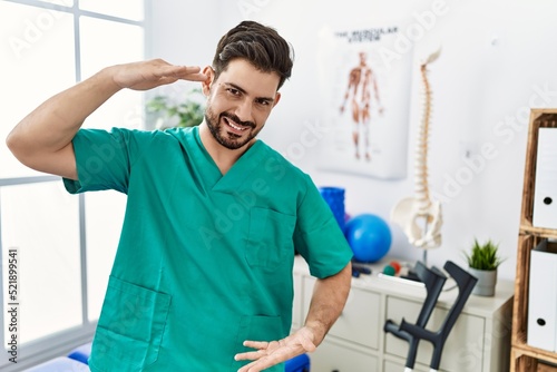 Young man with beard working at pain recovery clinic gesturing with hands showing big and large size sign, measure symbol. smiling looking at the camera. measuring concept.