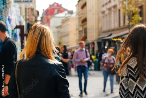 Defocus two stylish blonde and white women walking outdoors in autumn city street at sunset time wearing black jacket. View from the back. Friendship and travel. Out of focus