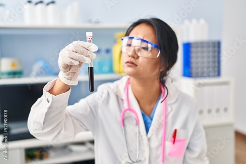 Young chinese woman wearing scientist uniform holding blood test tube at laboratory