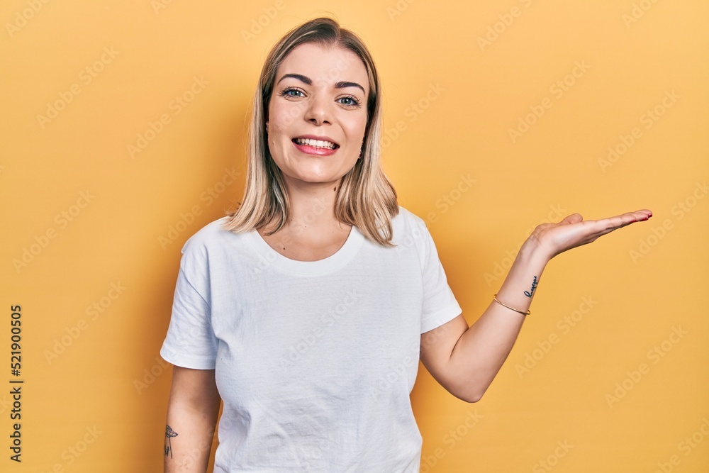 Beautiful caucasian woman wearing casual white t shirt smiling cheerful presenting and pointing with palm of hand looking at the camera. Beautiful caucasian woman wearing casual white t shirt smiling cheerful presenting and pointing with palm of hand looking at the camera.