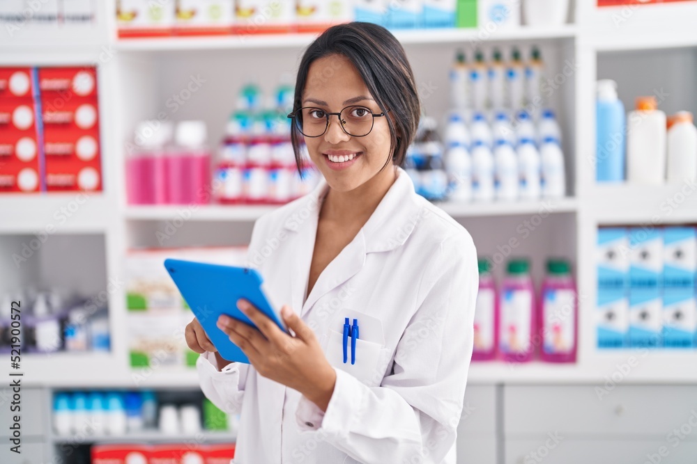 Young hispanic woman pharmacist using touchpad working at pharmacy
