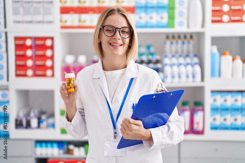 Young caucasian woman working at pharmacy drugstore holding pills winking looking at the camera with sexy expression, cheerful and happy face.