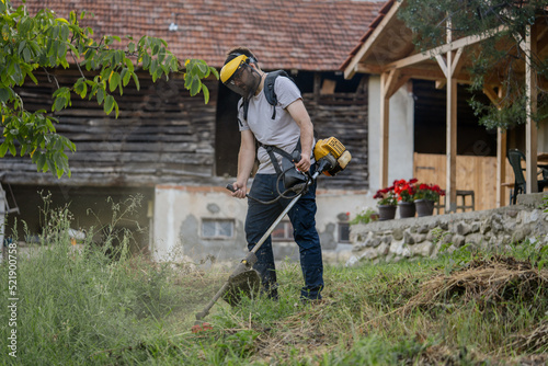 caucasian man farmer using string trimmer to cut grass brush cutter photo