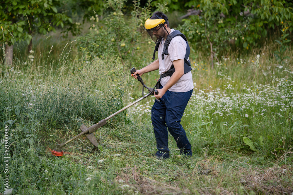 caucasian man farmer using string trimmer to cut grass brush cutter