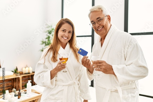 Middle age hispanic couple drinking champagne holding credit card at wellness center.