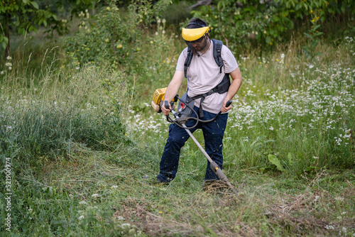 caucasian man farmer using string trimmer to cut grass brush cutter