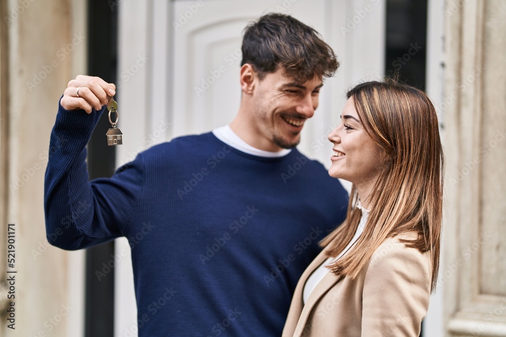 Naklejka premium Mand and woman couple hugging each other holding key of new home at street