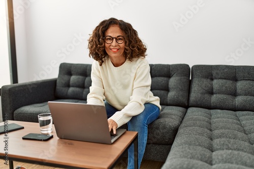 Middle age hispanic woman smiling confident using laptop at home