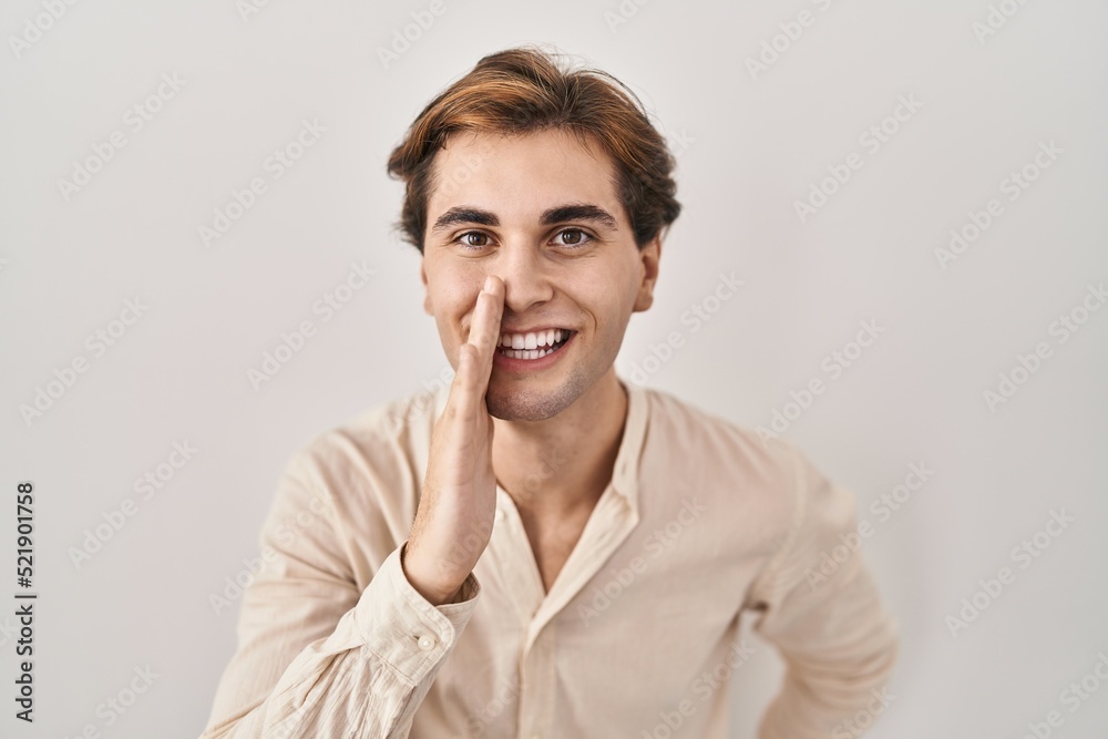 Young man standing over isolated background hand on mouth telling secret rumor, whispering malicious talk conversation Young man standing over isolated background hand on mouth telling secret rumor, whispering malicious talk conversation