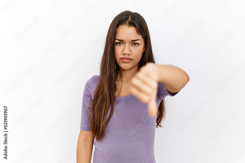 Young brunette woman standing by isolated background looking unhappy and angry showing rejection and negative with thumbs down gesture. bad expression. Young brunette woman standing by isolated background looking unhappy and angry showing rejection and negative with thumbs down gesture. bad expression.