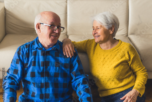 Relaxed beautiful loving senior family couple looking at each other, smiling and actively discussing something while sitting on the floor near the couch in the living room at home. High quality photo photo