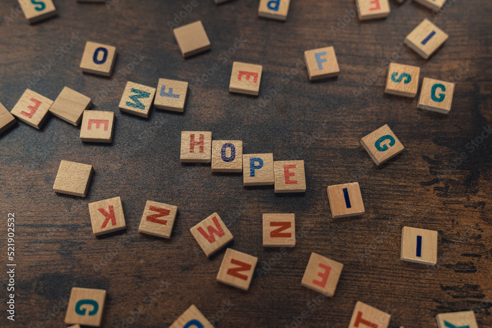Symbolic depiction of HOPE with the use of colourful wooden square letter puzzles. Dark wooden table as a background. Top view. High quality photo