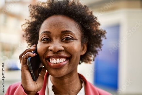 Beautiful business african american woman with afro hair smiling happy and confident outdoors at the city having a conversation speaking on the phone