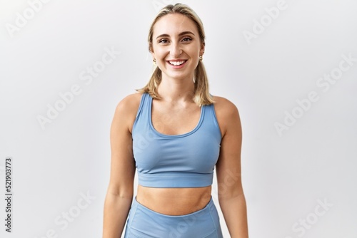 Young blonde woman wearing sportswear over isolated background looking positive and happy standing and smiling with a confident smile showing teeth